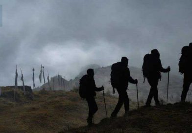 Fog‑covered mountain ridge at Tumling with silhouetted trekkers and prayer flags, reflecting the travel story by Srijit Das.