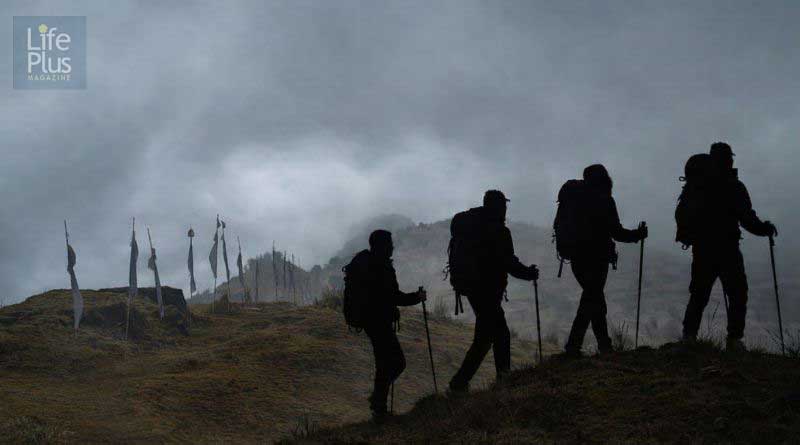 Fog‑covered mountain ridge at Tumling with silhouetted trekkers and prayer flags, reflecting the travel story by Srijit Das.